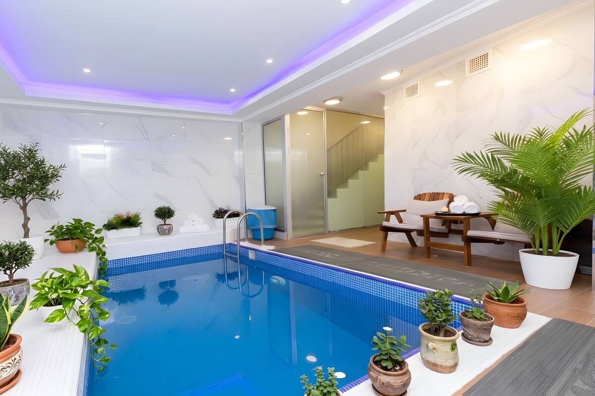 Une piscine intérieure moderne avec un mur en verre, des plantes en pot et un escalier menant à un niveau supérieur.