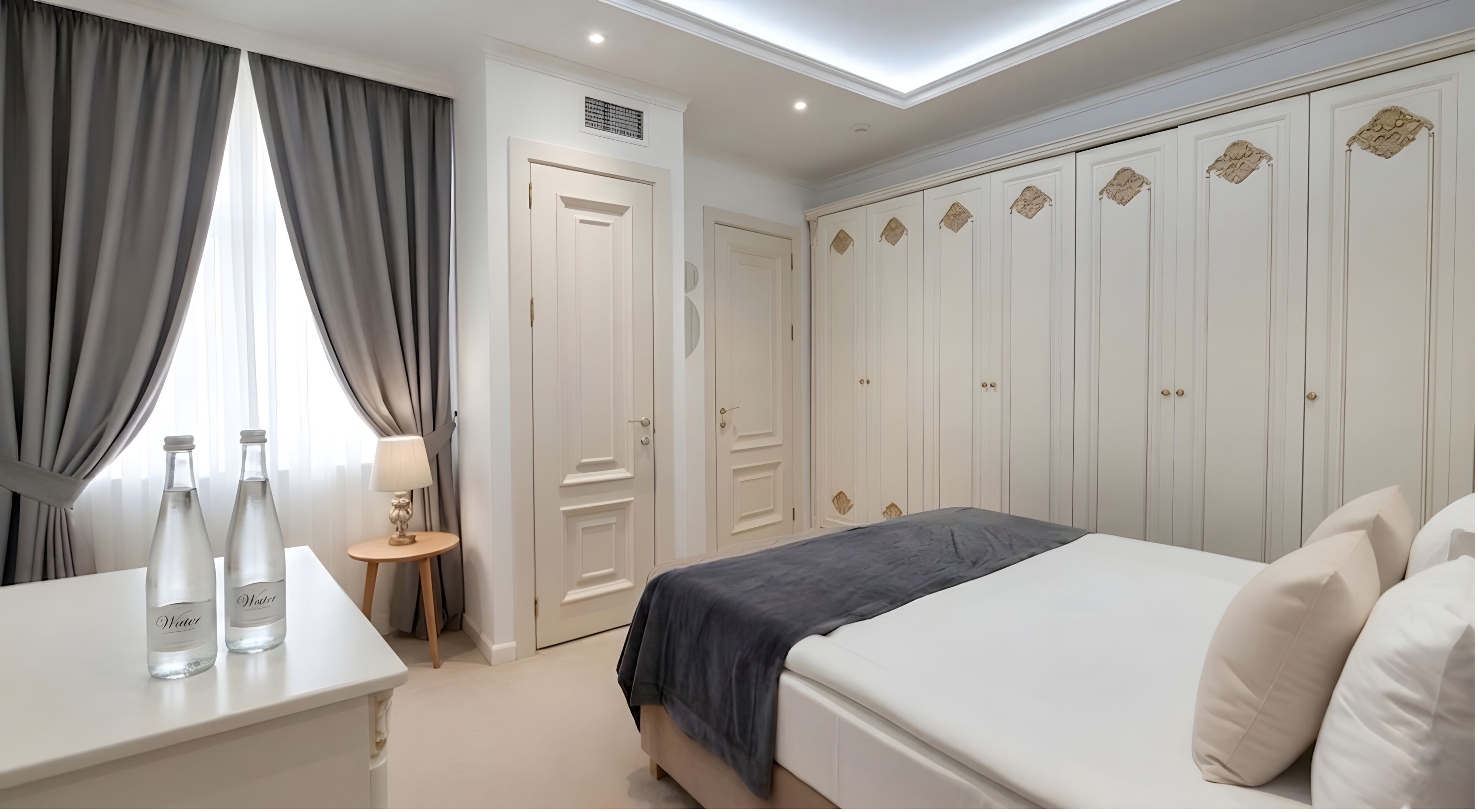 A bedroom with a bed, a nightstand with water bottles, a lamp, and a wardrobe.