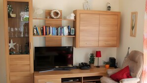 Un soggiorno con televisore, mobile porta TV in legno, scaffali, una lampada rossa, una poltrona e una decorazione a stella.