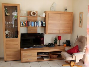 Ein Wohnzimmer mit Fernseher, einer Holz-Unterhaltungsecke, Bücherregalen, einer roten Lampe, einem Sessel und einer Sternen-Dekoration.
