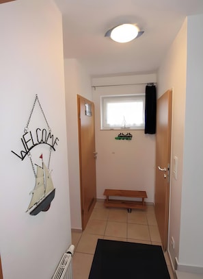 Ein Korridor mit einem 'WELCOME'-Schild, einer Bank, einem Fenster und einer Tür.