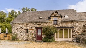 Ein Steinhaus mit einer roten Tür, einem kleinen Fenster und einem großen Fenster.
