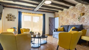 Ein Wohnzimmer mit freiliegenden Holzbalken, einer Couch, gelben Sesseln, einem Couchtisch und einer Wand mit Musterpapier.