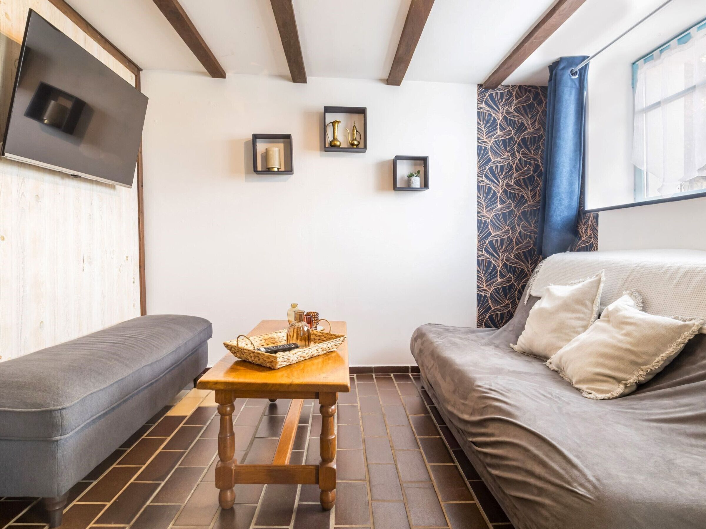 Een gezellige kamer met een bank, een klein houten tafeltje, een aan de muur bevestigde televisie en een kamerbreed gordijn.