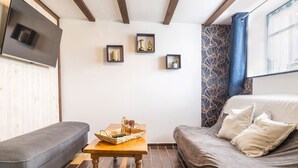 Una habitación acogedora con un sofá, una pequeña mesa de madera, un televisor montado en la pared y una cortina estampada.