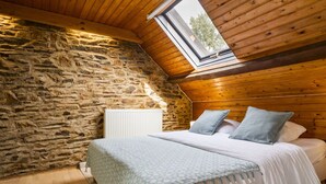 Un dormitorio con pared de piedra, techo de madera, una cama con almohadas y una ventana.