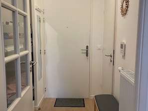 Ein schmaler Flur mit einer geschlossenen Tür, einem Heizkörper und einem Thermostat an der Wand.