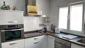 Una cocina moderna con armarios blancos, electrodomésticos de acero inoxidable y un ventanal que proporciona luz natural.