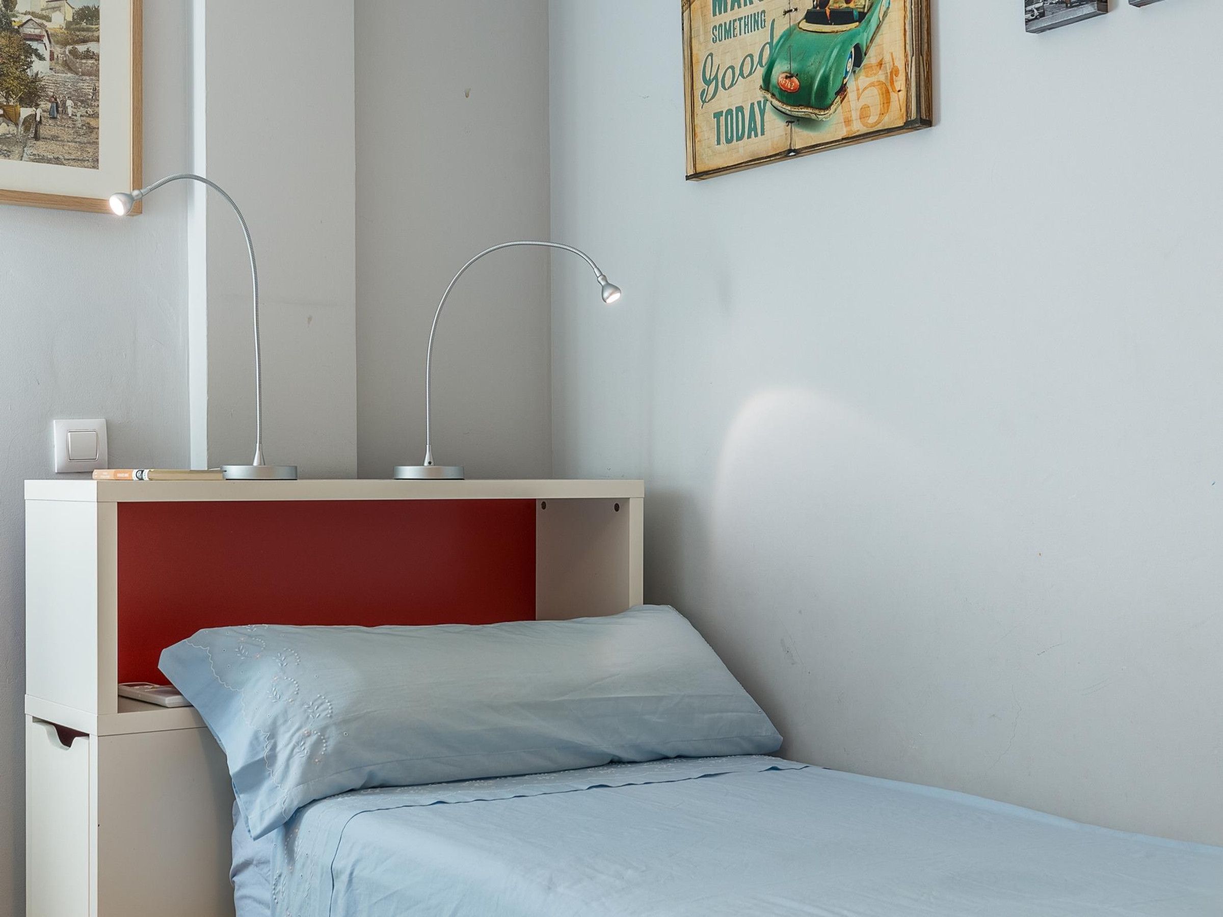 Ein Schlafzimmer mit einem Einzelbett, einem Schreibtisch mit zwei Lampen und einem Wandbild.