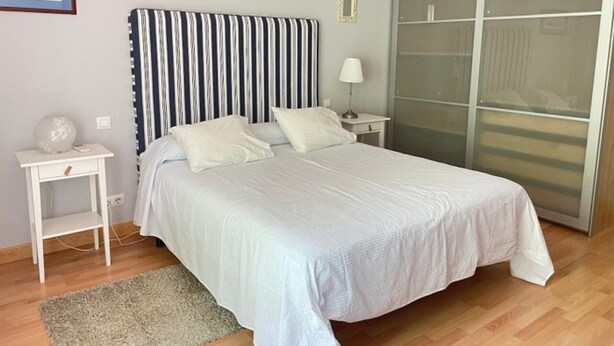 Un dormitorio con cama, mesita de noche, lámpara y armario.