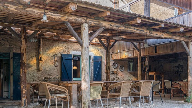 Una estructura de madera al aire libre con una mesa y sillas, un interior rústico con techo de madera y una pared de piedra.