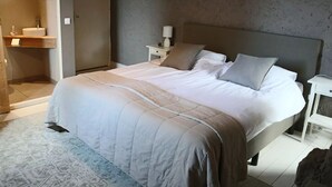 Un dormitorio con cama, mesitas de noche, tocador y baño con lavabo e inodoro.