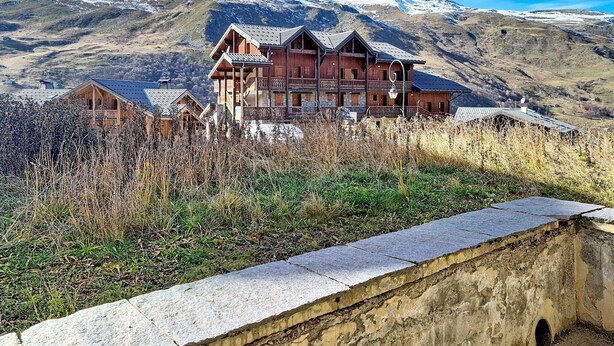 A multi-story wooden chalet with balconies, set against a mountainous backdrop. - Spacious apartment near slopes with balcony (Les Menuires)