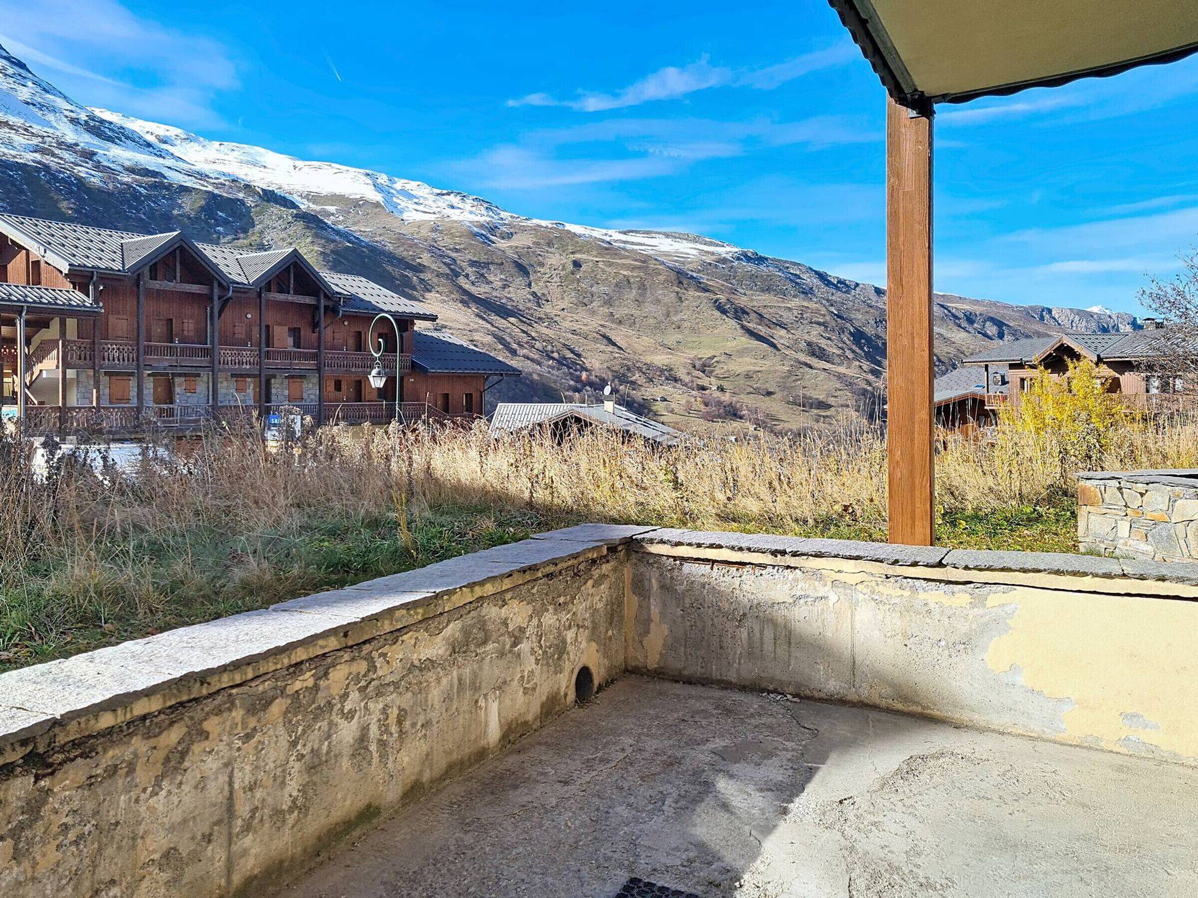Een berghut met balkon, een stenen muur en uitzicht op besneeuwde bergen.