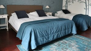 Uma cama de casal com colcha azul, duas mesas de cabeceira com luminárias, parede com mural de bambu e tapete estampado sobre piso de madeira.
