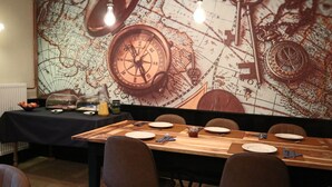 Uma área de refeições com uma mesa comprida posta para quatro pessoas, um mural de mapa antigo na parede e uma bússola antiga.
