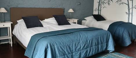 Cama doble con cubrecama azul, dos mesitas de noche con lámparas, pared con un mural de bambú y alfombra estampada.