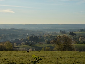 A rural landscape with rolling hills, a church spire, and a deer in a field.