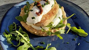 A blue plate with a food item topped with greens and a creamy substance.