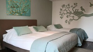 A double bed with two pillows, a nightstand, a wall-mounted tree decal, and a patterned rug.