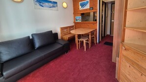 Ein Zimmer mit einer schwarzen Ledersofa, einem Holztisch mit Stühlen, einer Holzkommode und einer Uhr an der Wand.