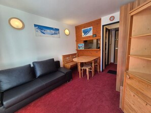 Ein Zimmer mit einer schwarzen Ledersofa, einem Holztisch mit Stühlen, einer Holzkommode und einer Uhr an der Wand.