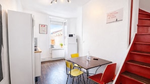 A compact kitchen with a dining area, a red staircase, and a view of the outside. - La Maison Créative (La Madeleine)