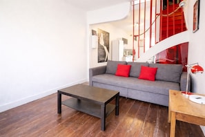 A modern living room with a grey sofa, red cushions, a wooden coffee table, and a red staircase. - La Maison Créative (La Madeleine)