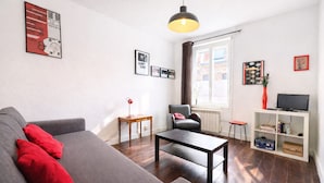 A living room with a sofa, coffee table, chair, and a TV stand with books. - La Maison Créative (La Madeleine)