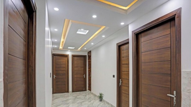 Un pasillo con puertas de madera, suelo de mármol e iluminación empotrada.