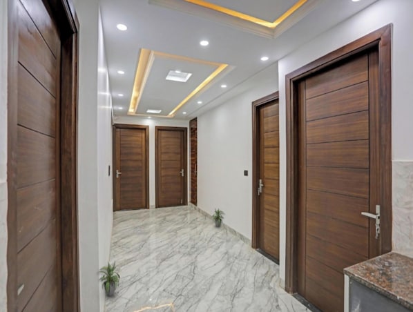 A hallway with wooden doors, marble flooring, and recessed lighting. - Quadis Central  (Noida)