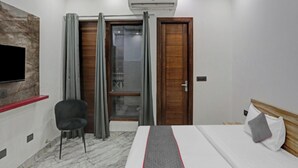 Habitación de hotel con cama, televisor montado en la pared, silla, puerta de madera y equipo de aire acondicionado.