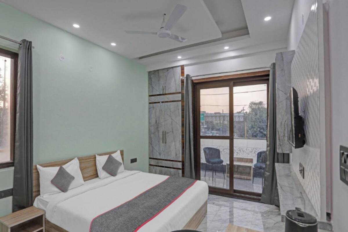 Una habitación de hotel con cama, escritorio, silla, televisor y balcón con sillas.