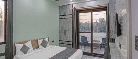 A hotel room with a bed, a desk, a chair, a TV, and a balcony with chairs.
