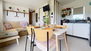 Un espacio habitable compacto con zona de comedor, kitchenette y sofá decorado con cojines.