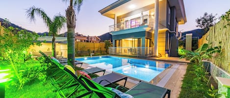 A modern house with a swimming pool, lounge chairs, and a balcony overlooking the pool.