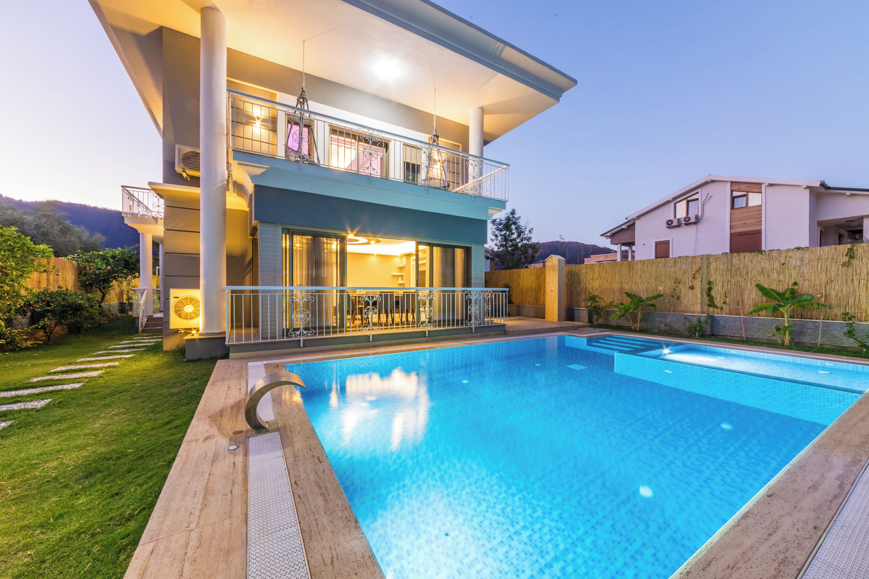 A modern two-story house with a swimming pool, a balcony with outdoor furniture, and a well-maintained garden.
