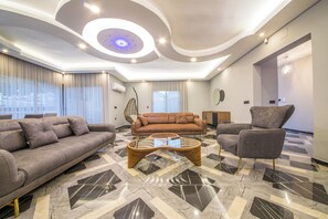 Ein modernes Wohnzimmer mit Sofa, Sessel und Couchtisch, mit einem einzigartigen Deckengestaltungsstil und gemustertem Boden.