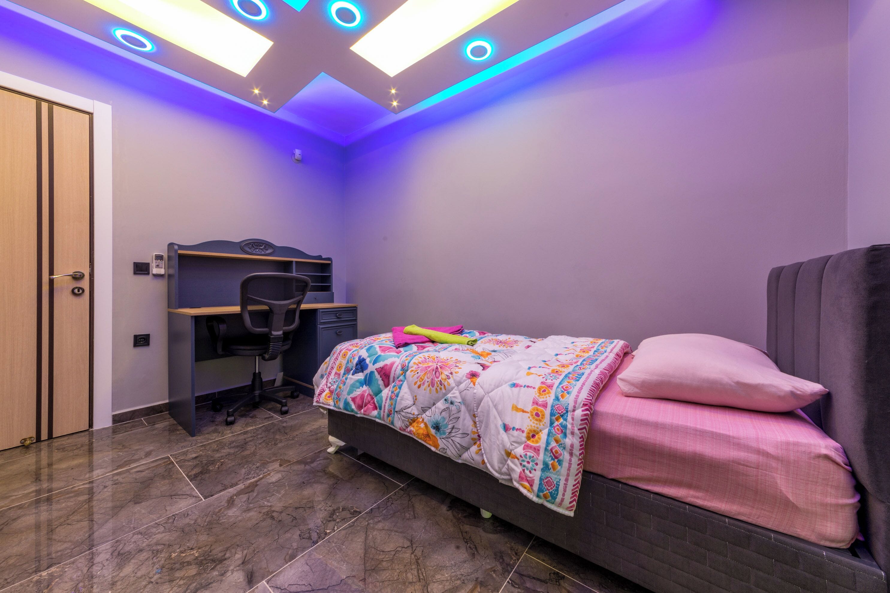 A bedroom with a bed, desk, and chair, featuring a modern ceiling design with circular lights.