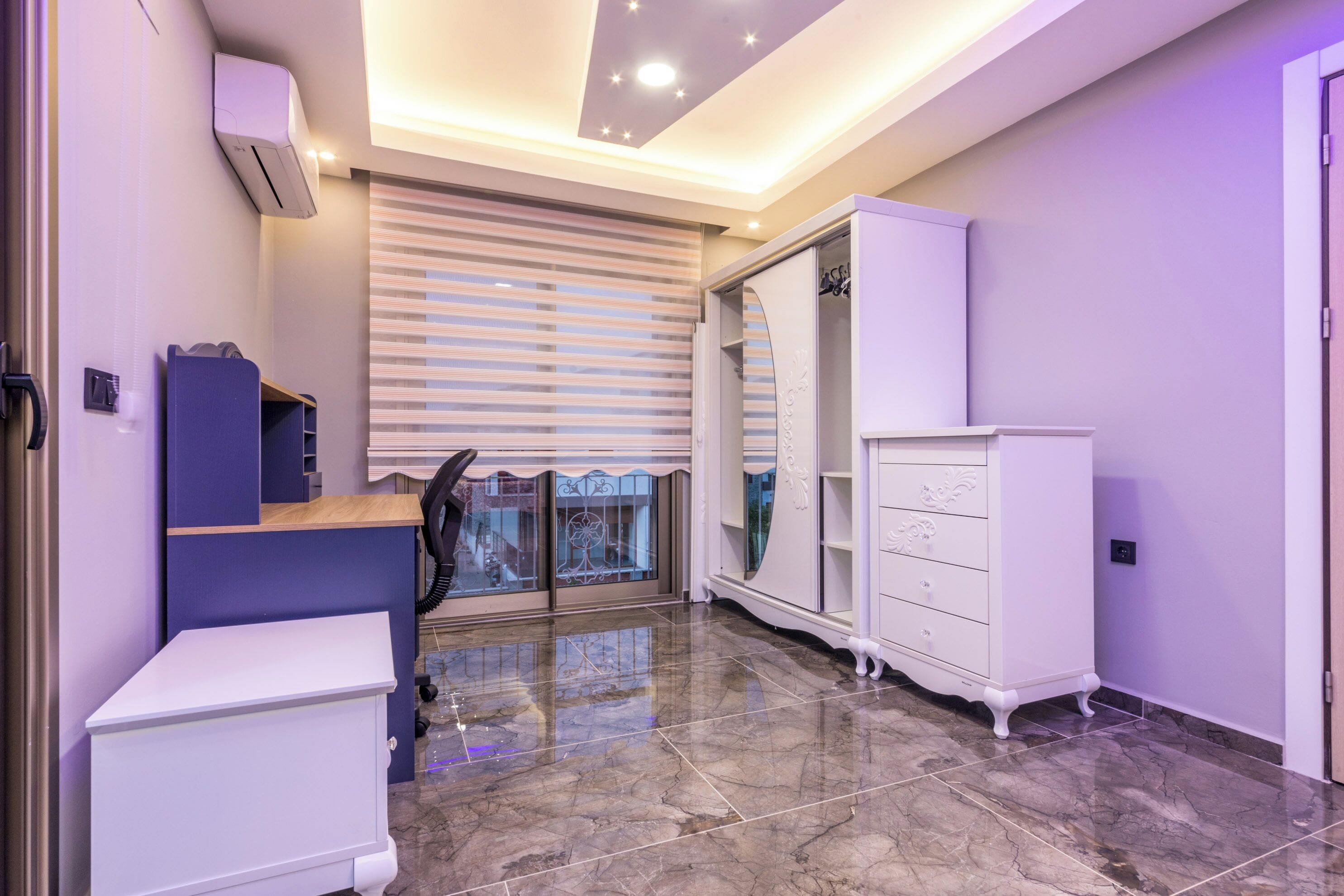 A modern room with a desk, wardrobe, and a large window with blinds.