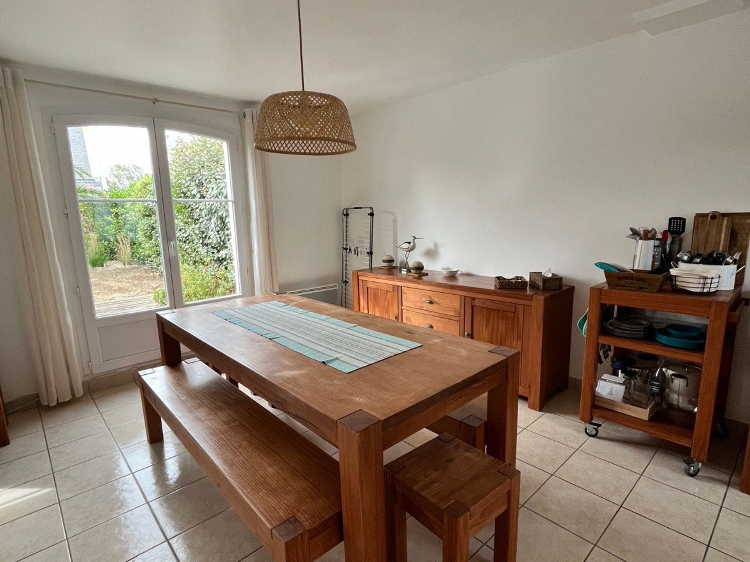 A kitchen with a wooden table, bench, and a hanging light fixture.