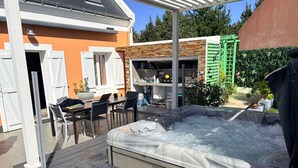 A hot tub on a wooden deck, a covered outdoor seating area, and a brick building with a green gate. - Family house with pets - 8 guests (Le Palais)
