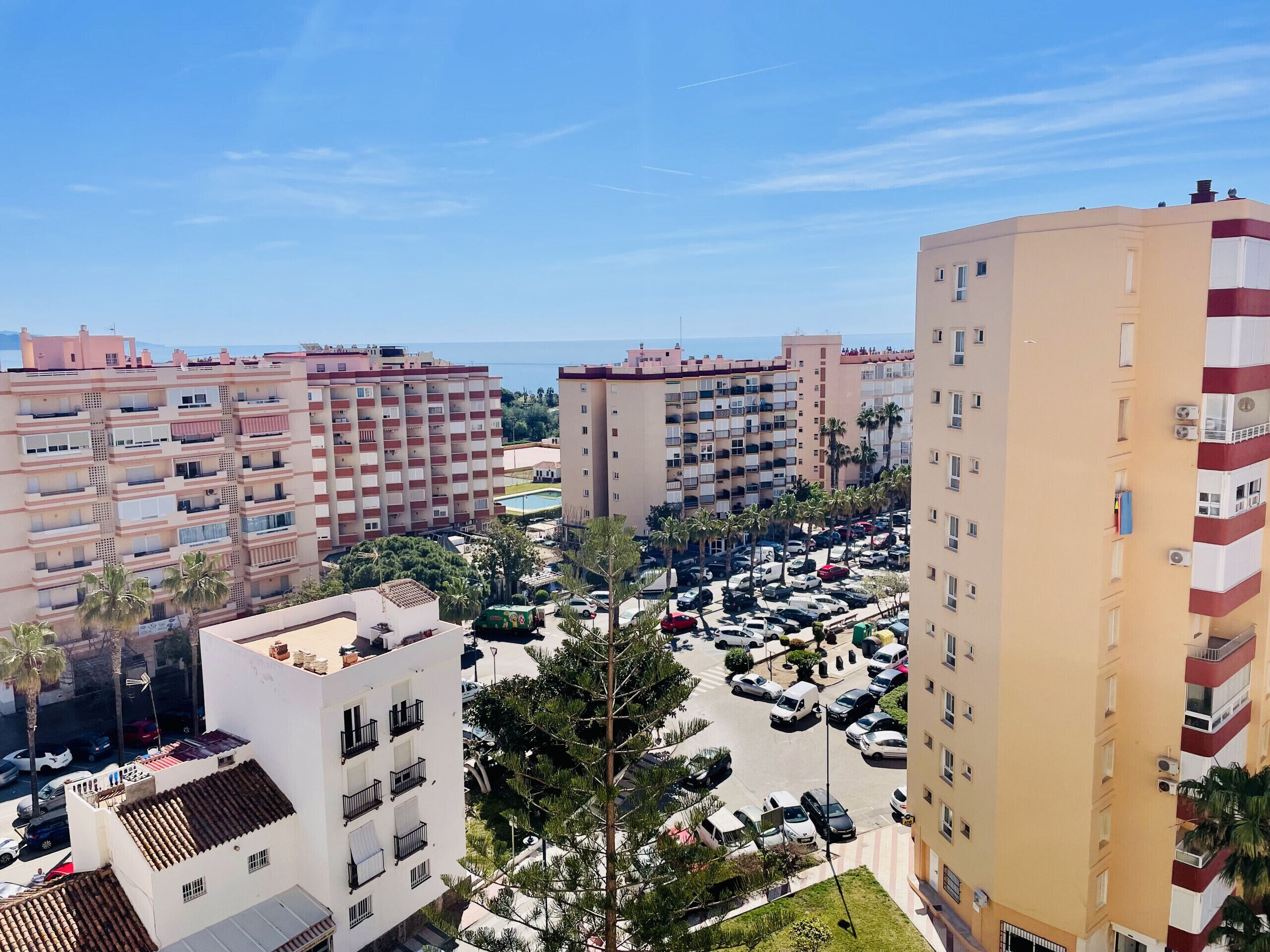A high-rise residential building with multiple balconies, a parking lot, and a view of the sea.