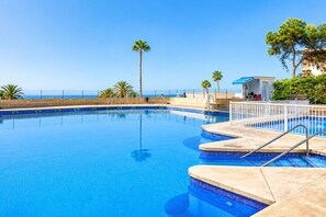 A swimming pool with steps leading into it, surrounded by palm trees and a view of the ocean. - Lighthouse 77 Apartment by At Home Costa del Sol (Torrox)