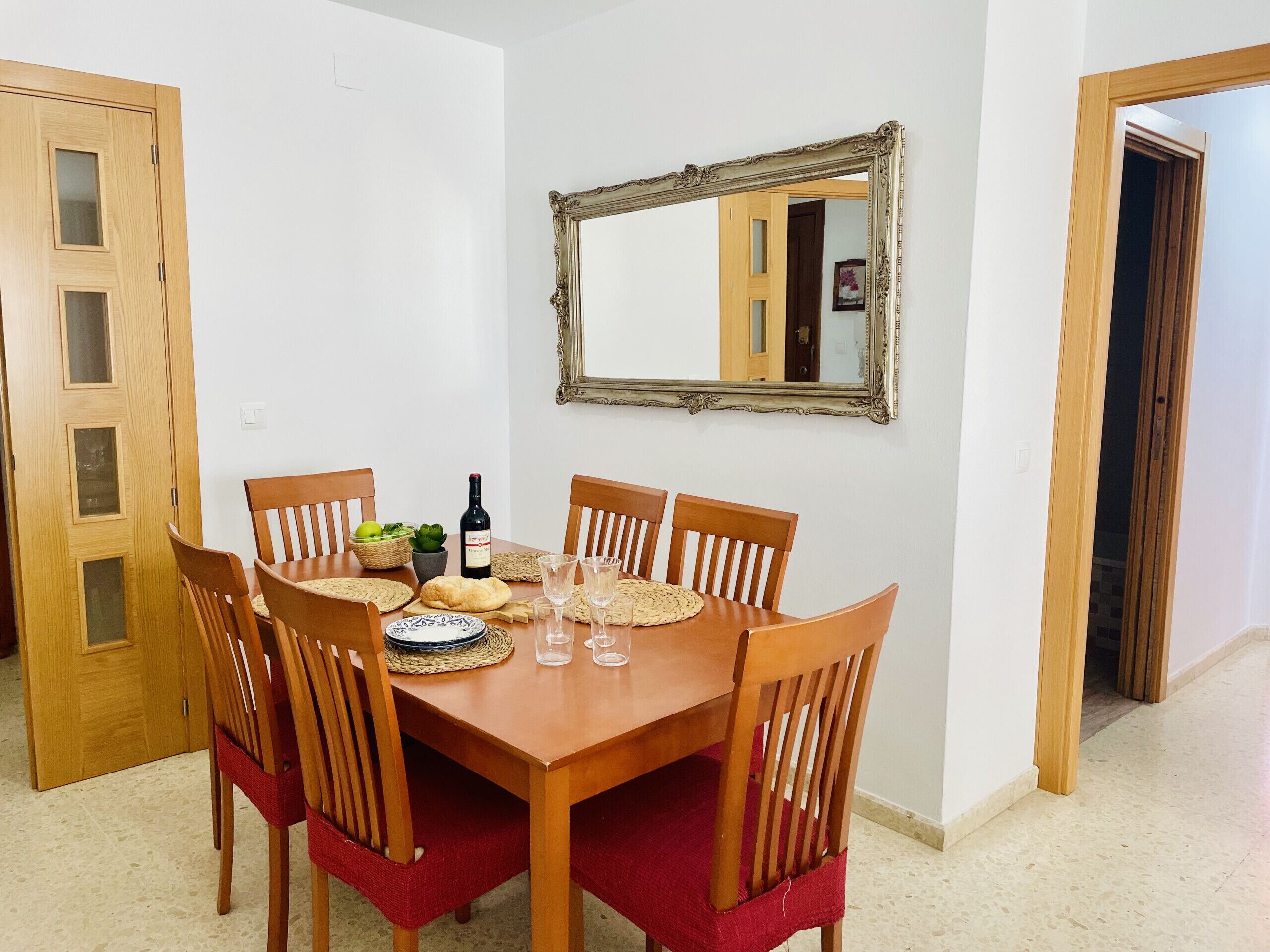 Une table à manger avec des chaises, une bouteille de vin, des verres et un miroir au mur.