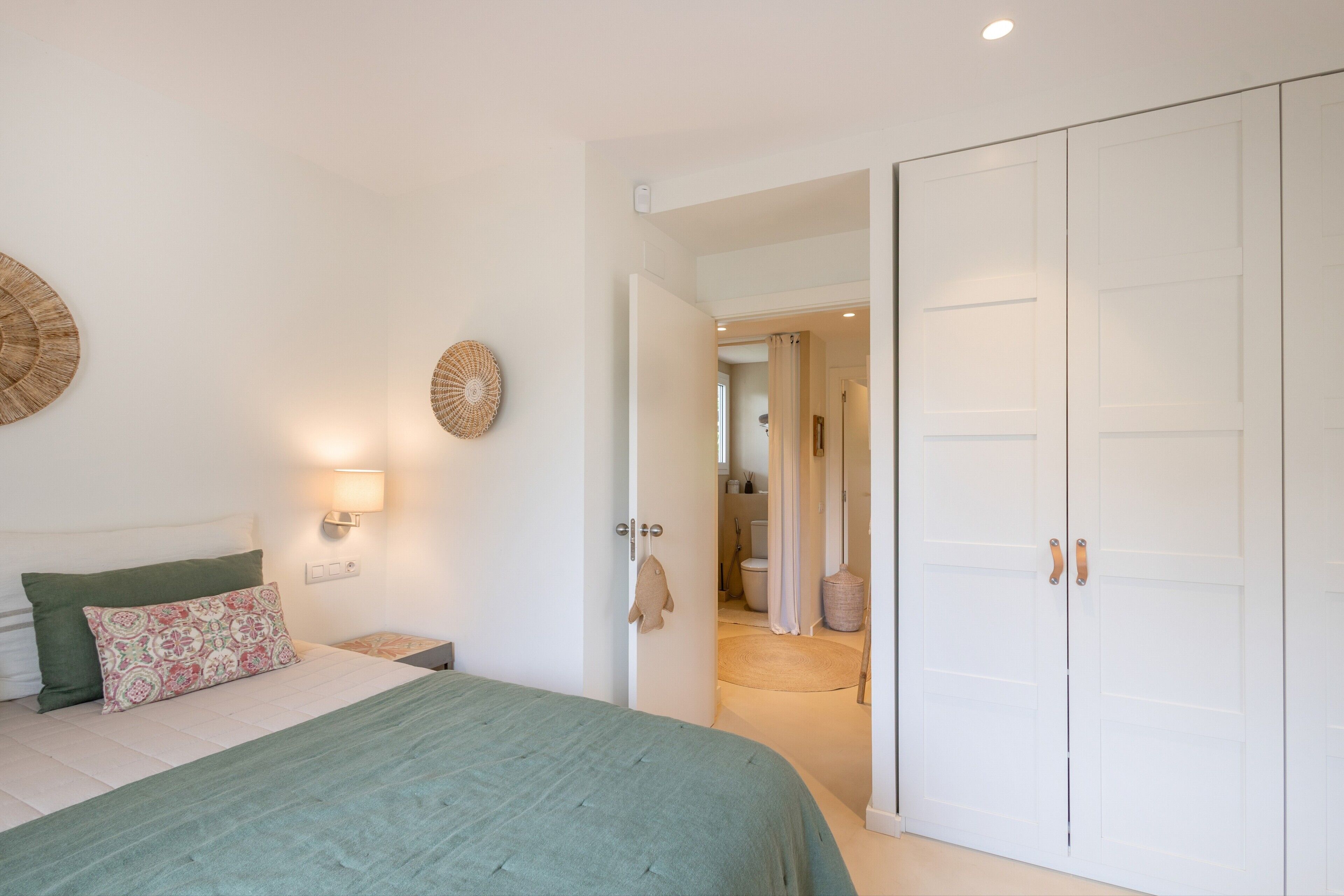 A bedroom with a bed, bedside tables, a wardrobe, and a bathroom visible through an open door.