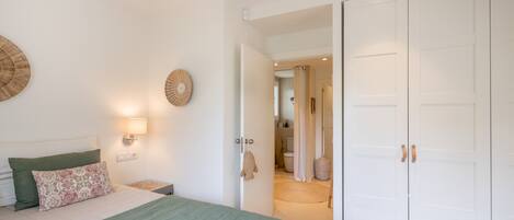 Une chambre à coucher avec un lit, des tables de chevet, une armoire et une salle de bain visible à travers une porte ouverte.