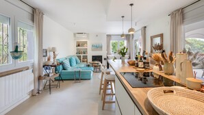 A modern kitchen with a central island, bar stools, and a dining area with a blue sofa. - Villa with Pool Just 500 Meters from the Beach (Begur)
