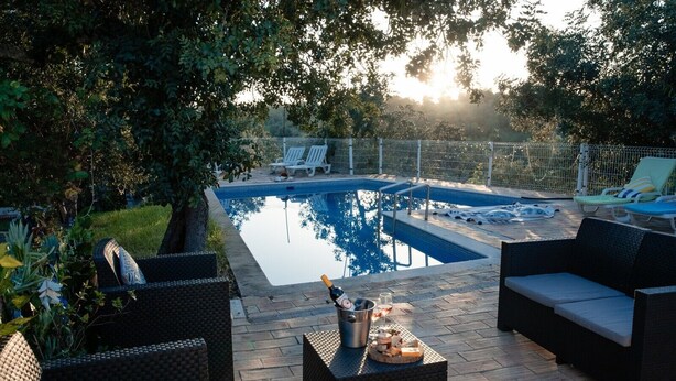 A pool area with lounge chairs, a table with drinks, and a fenced swimming pool.