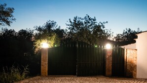 A gated entrance with a cobblestone driveway leading to a building with a stone wall.